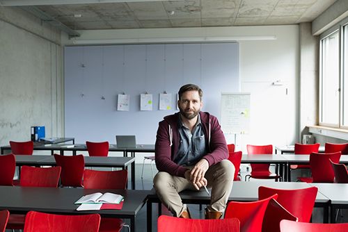 Educator sitting on desk in an empty classroom Educator sitting on desk in an empty classroom