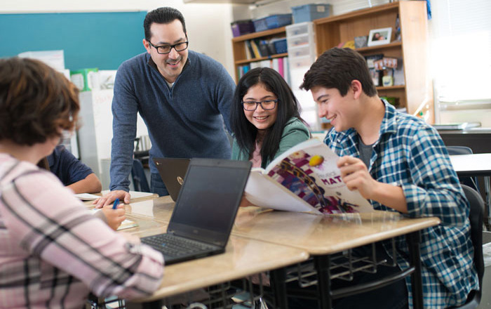 High school students working collaboratively with teacher helping them High school students working collaboratively with teacher helping them