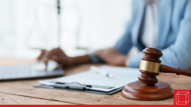Gavel on a table with person on laptop in background