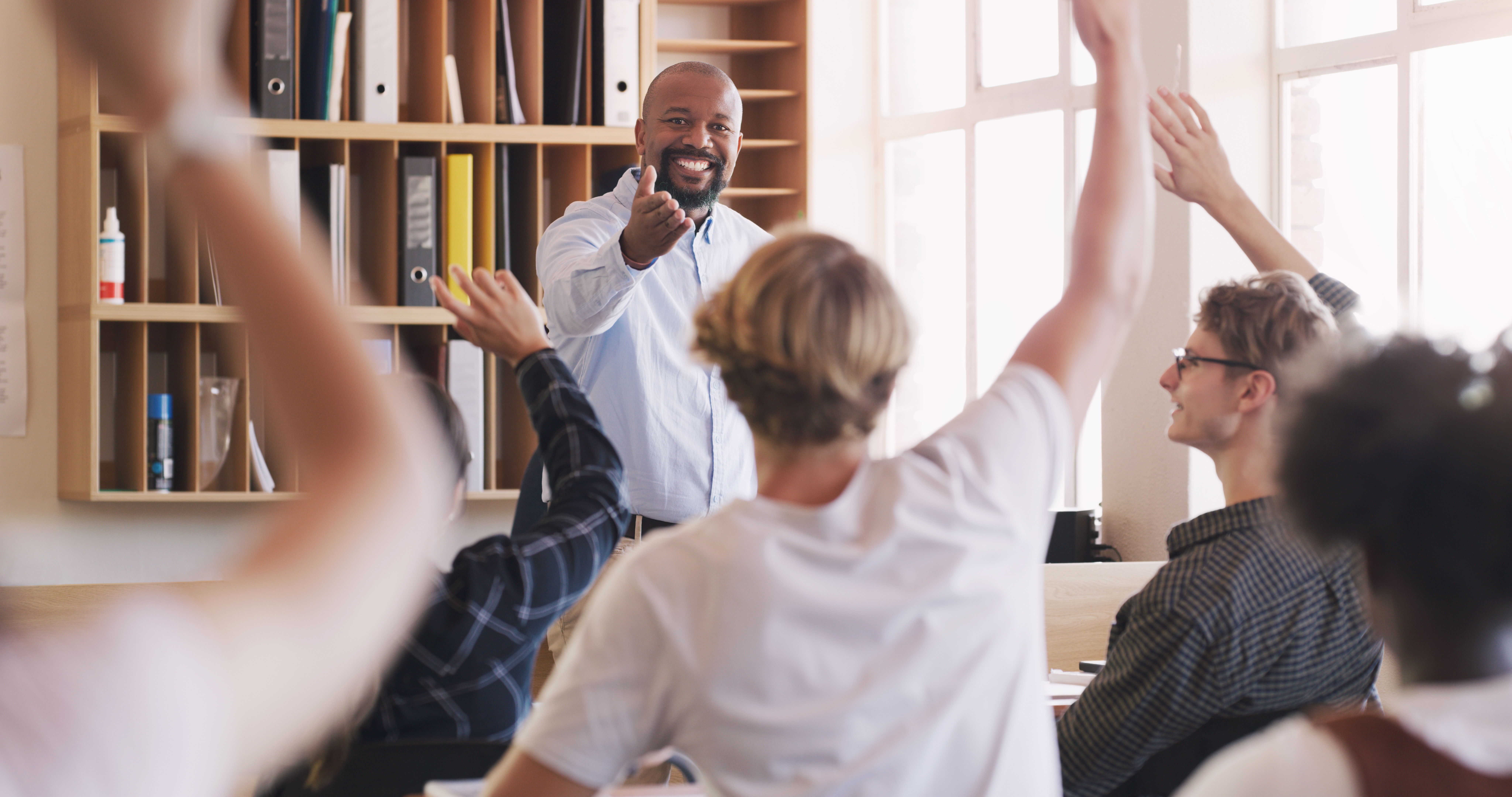 Teacher, man and student hands and question in classroom for teaching, learning and education with answer. Happy, male professor and school for lesson, feedback or knowledge for academic test.