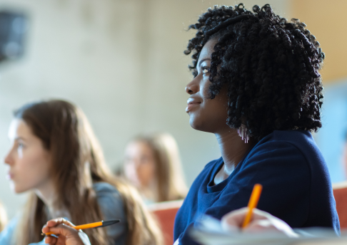 A woman looks attentively in class while holding a pencil.