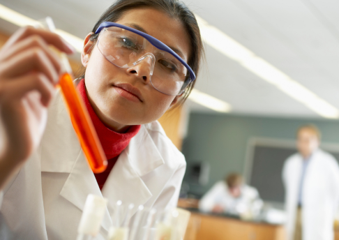 A woman in a science class studies a beaker filled with liquid.