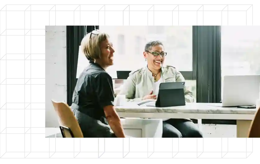 Two women sitting at a table with devices.