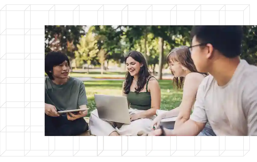 Group of students sitting outside on devices.