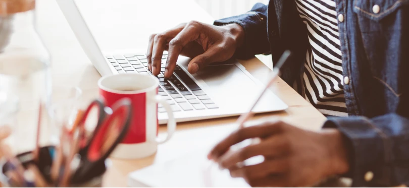 Image of person in front of laptop writing on a piece of paper.