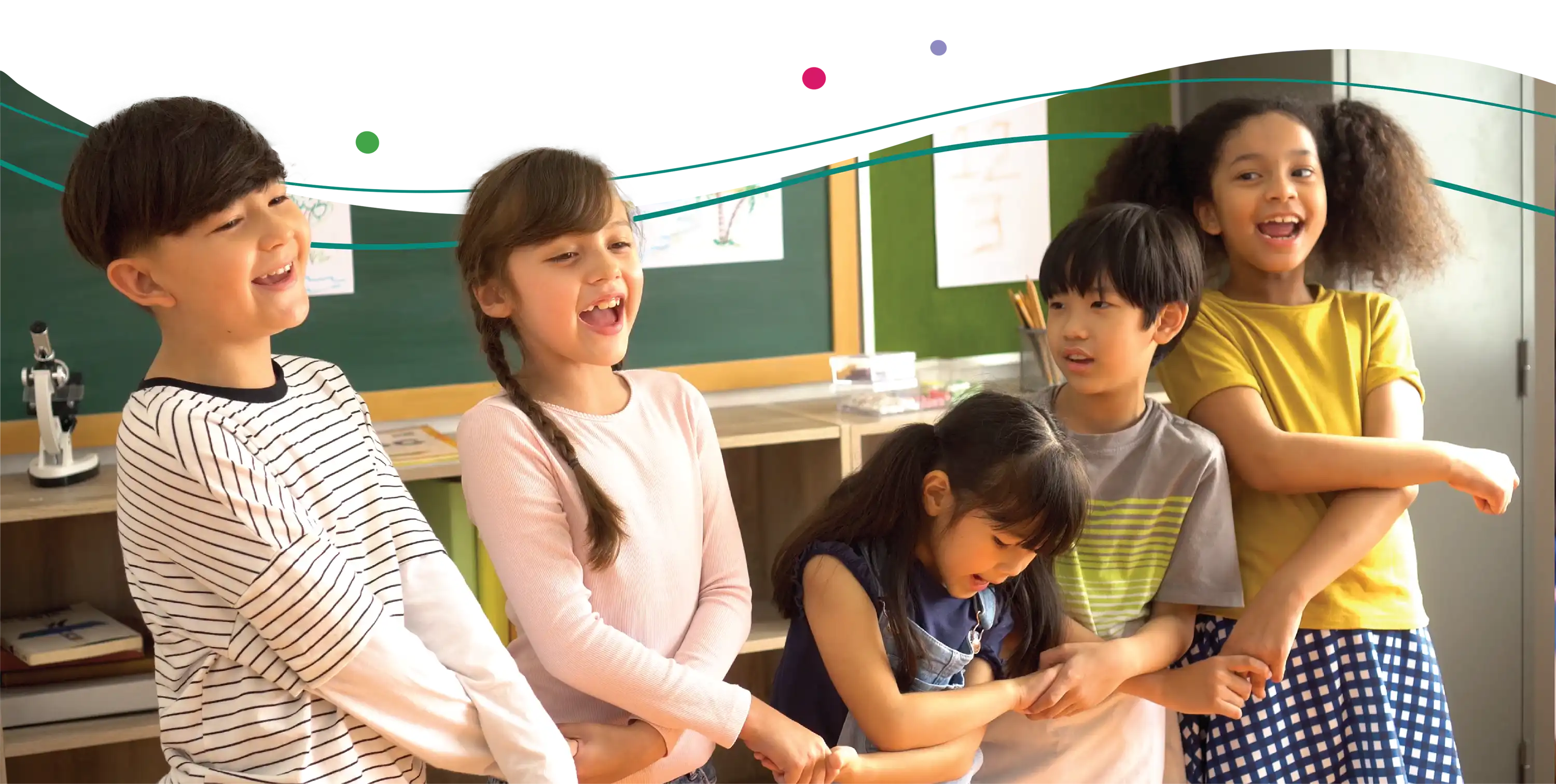 Five smiling children hold hands in a classroom.