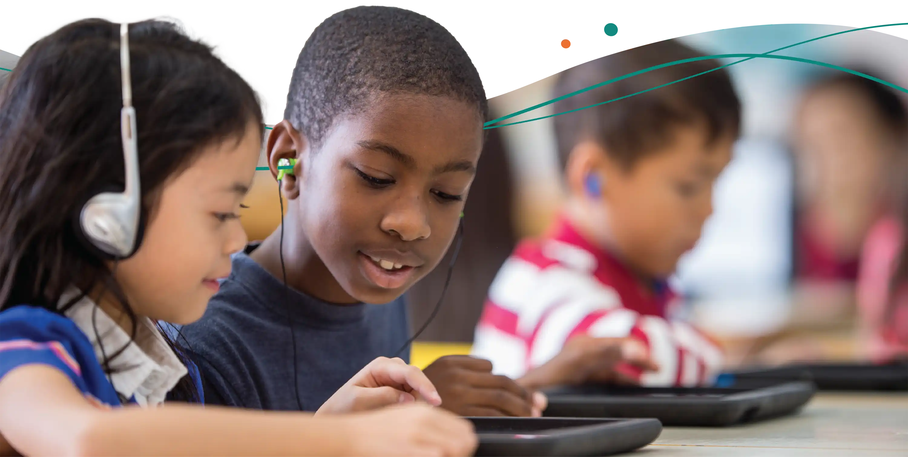 students sitting at table using tablets and wearing headphones