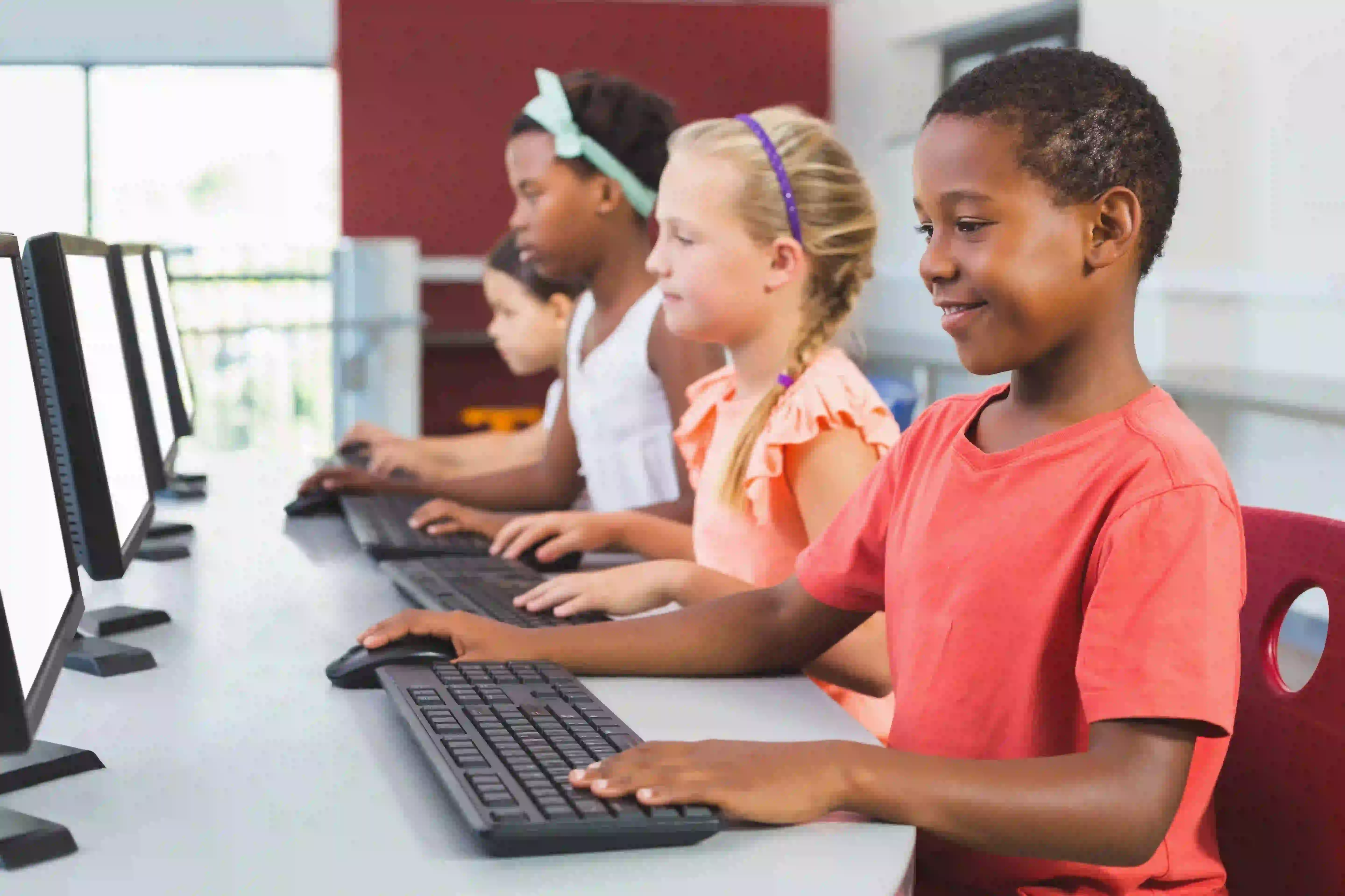 A group of four young students work on computers in a row.