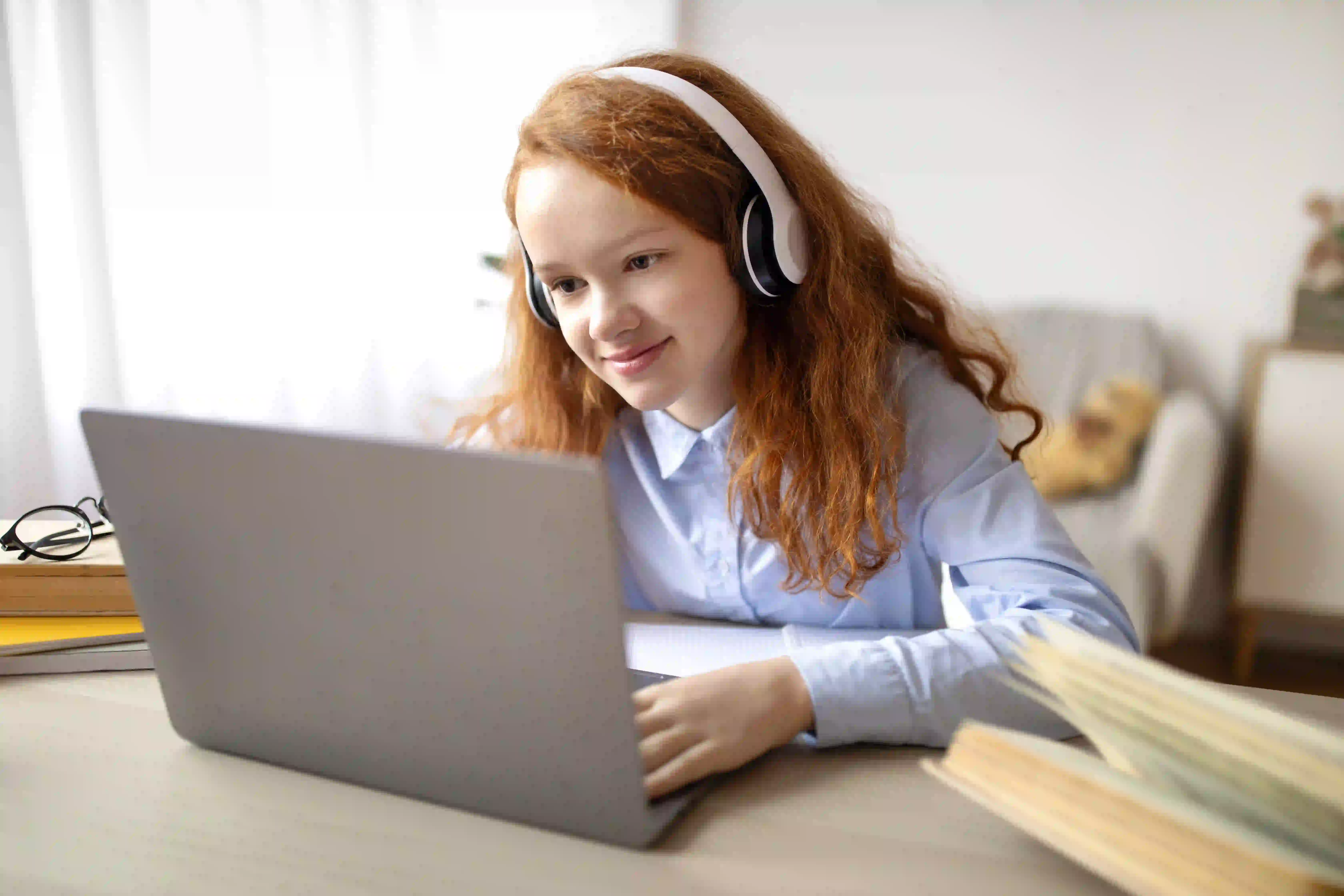 A young girl wearing over-ear headphones looks contentedly at a laptop.