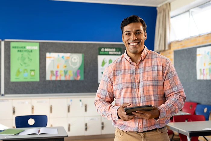 Portrait of happy biracial male teacher with tablet in classroom at elementary school, copy space. School, learning, communication, teaching and education, unaltered.; Shutterstock ID 2528747989; purchase_order:DPG Bulk Purchase Jul/Aug 2025; job:DPG selections; client:McGraw Hill; other: